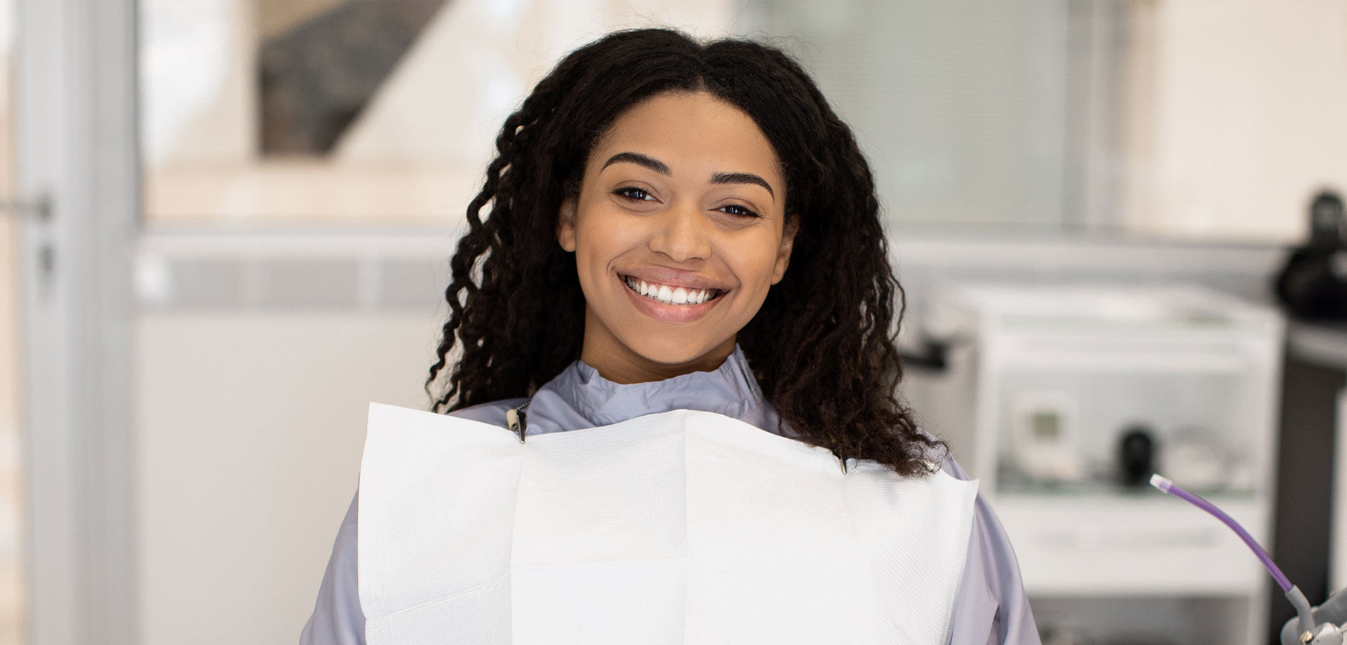 A woman in a dental office, smiling and holding up a sign with a price list.