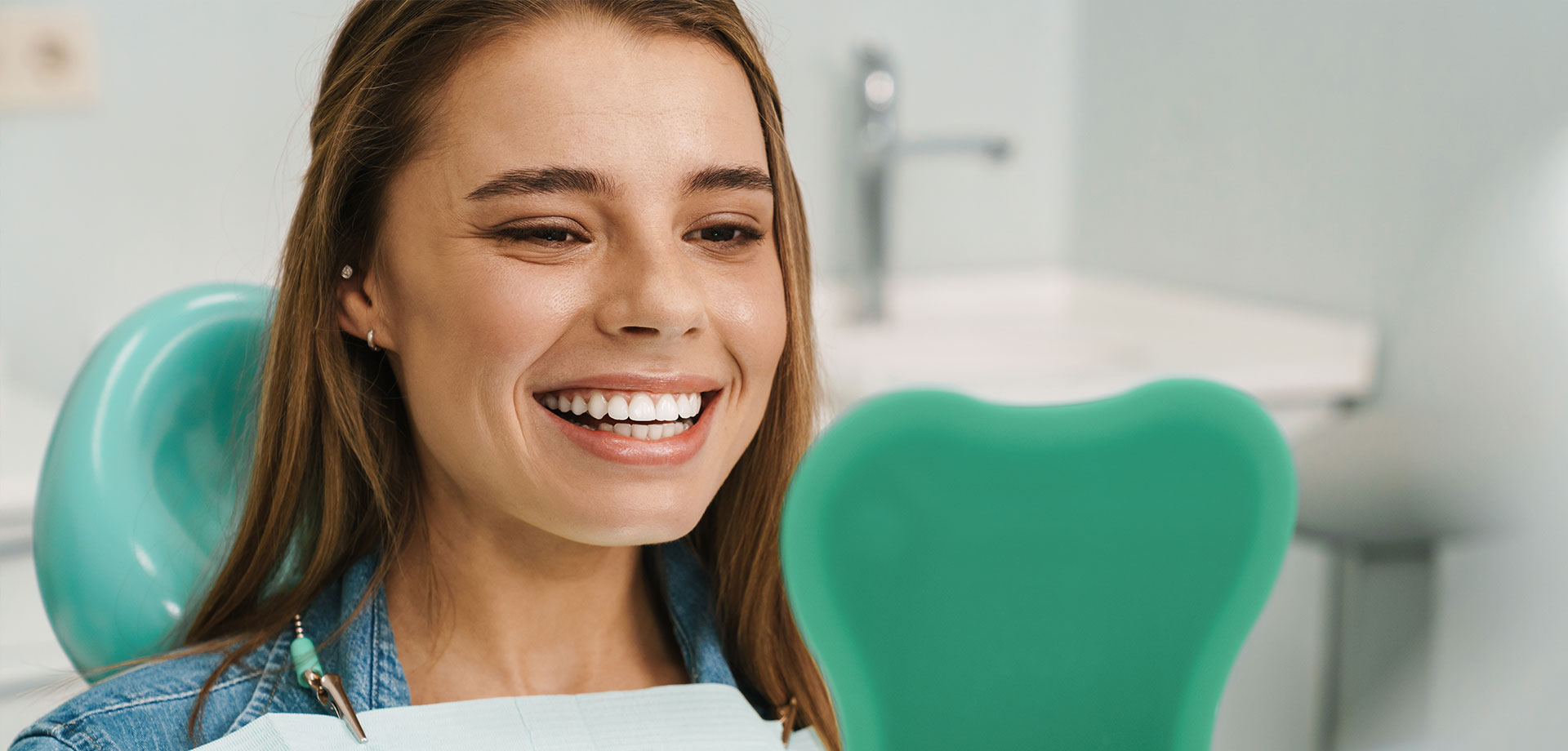 Smiling woman in a dental office, holding up a green mouthguard for display.