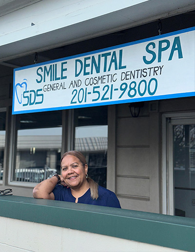 A woman stands in front of a sign advertising a dental spa, with the text  SMILE DENTAL SPA  visible.