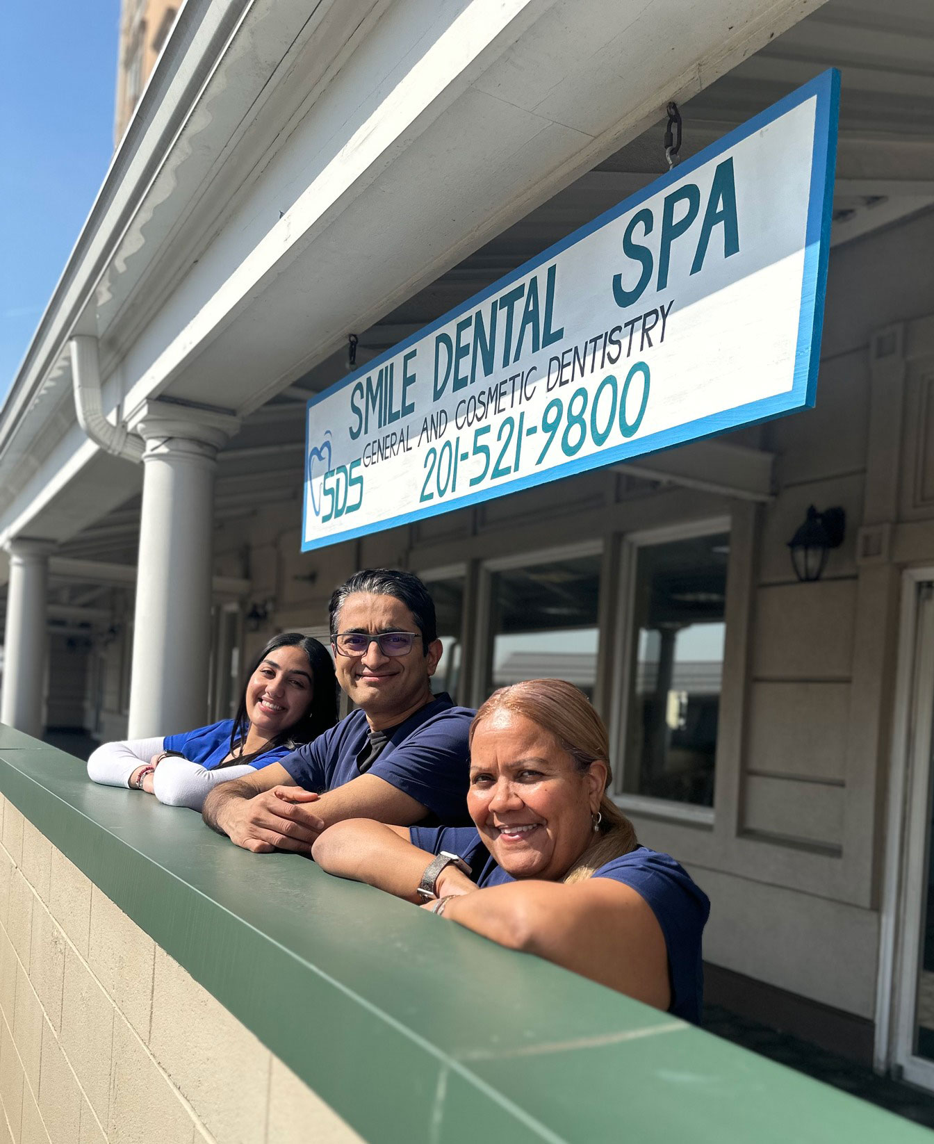 The image shows three individuals leaning against a railing in front of a building with a sign that reads  Smile Dental Spa.