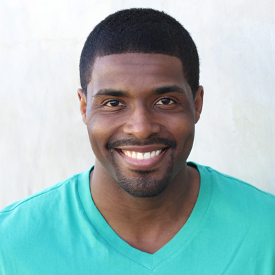 A man and a woman, both smiling, pose closely together outdoors.