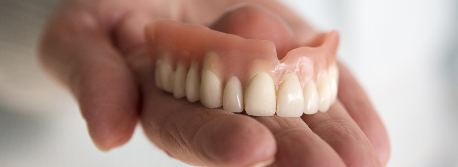 The image shows a person holding an artificial human mouth with teeth, likely for dental prosthetics or educational purposes.