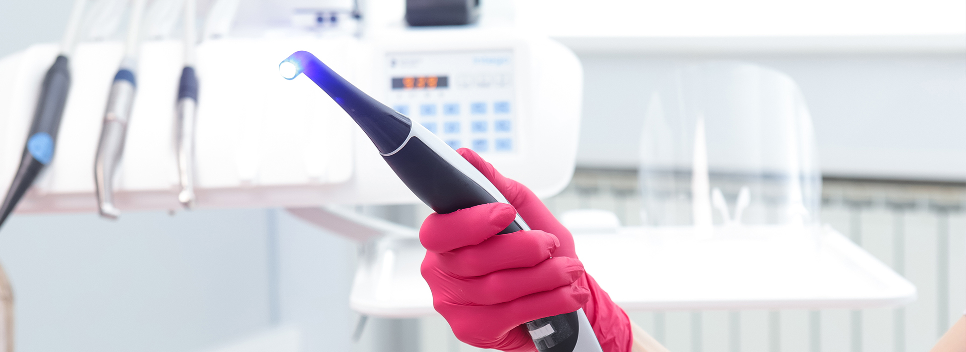 A person holding a blue device in their hand, wearing pink gloves and standing in front of a medical equipment cabinet.