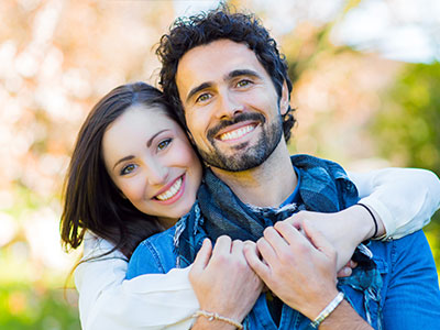 The image shows a man and woman in a close embrace, smiling and looking at the camera.