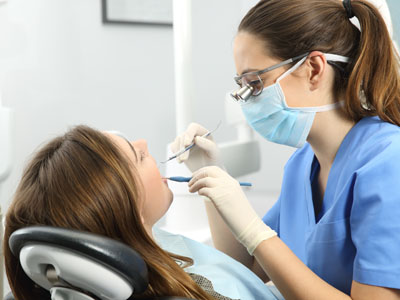 The image shows a dental professional performing oral care on a patient, with the dentist wearing protective eyewear and using dental instruments.