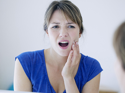 A woman with a concerned expression, looking into the mirror while holding her hand to her mouth.