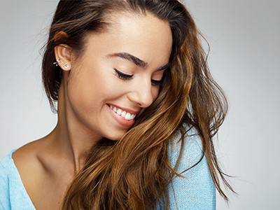 The image is a portrait of a smiling woman with long hair, wearing a blue top and earrings.