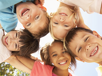 A group of children, both boys and girls, smiling and posing for a photo with their arms around each other.