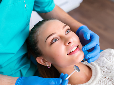 The image shows a woman receiving dental care, with a dentist performing a procedure while she smiles and looks at the camera.