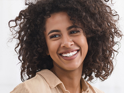 The image shows a smiling woman with curly hair, wearing a light-colored top and looking directly at the camera.